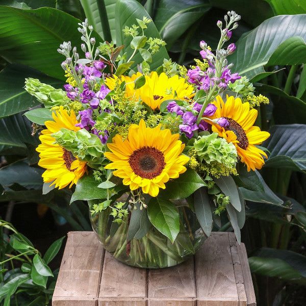 Sunflower bouquet in a clear glass vase with purple flowers