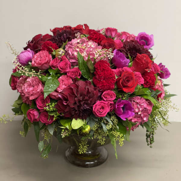 Low, lush arrangement of red and pink flowers in a clear glass pedestal bowl