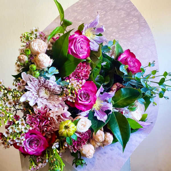 Bouquet of pink roses, lavender flowers, and mixed blooms wrapped in pale paper
