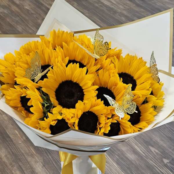 Bouquet of yellow sunflowers wrapped in white paper with gold trim