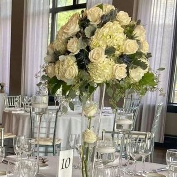 Tall cream rose centerpiece in a clear glass vase on a banquet table