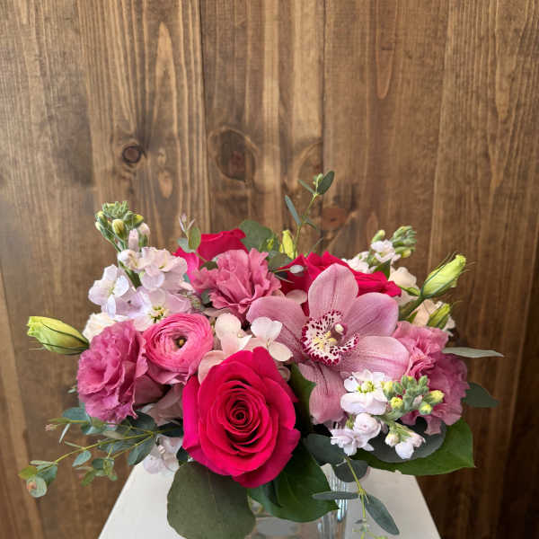Pink and white bouquet with roses and orchids in a square glass vase