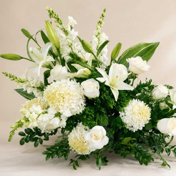 White lilies and roses arranged with round white blooms in a low display.