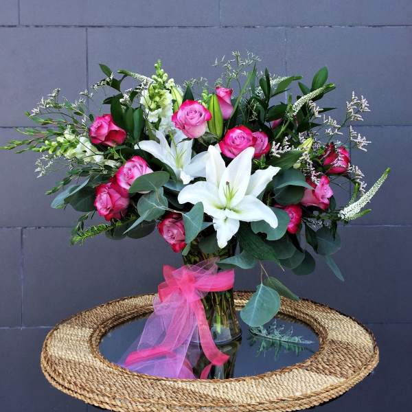 Pink roses and white lilies in a glass vase with a pink ribbon