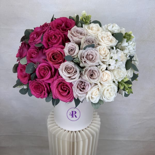 Round hatbox arrangement of pink, lavender, and white roses in a white container