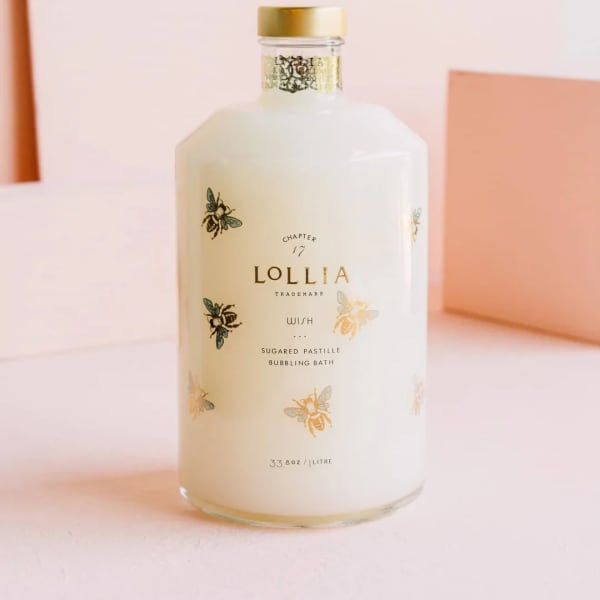 White bottle of Lollia bath product with gold cap and bee illustrations