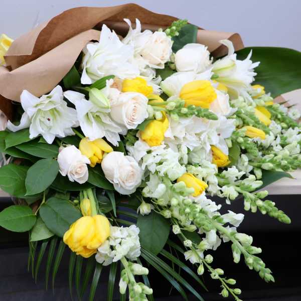 Wrapped bouquet of white lilies, cream roses, and yellow tulips with trailing white snapdragons