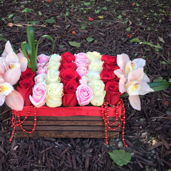 Rectangular floral arrangement with red, pink, and white roses and pale orchids in a wooden box