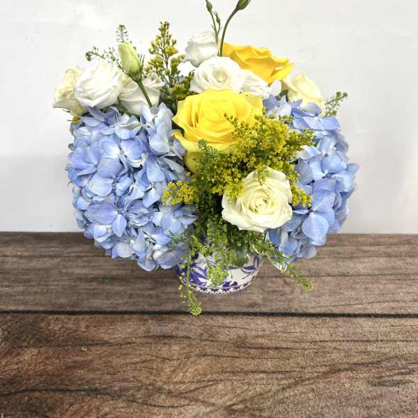 Blue hydrangeas with yellow and white roses in a small vase