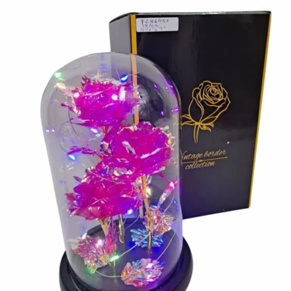 Artificial pink roses with LED lights inside a glass dome on a black base beside a black gift box