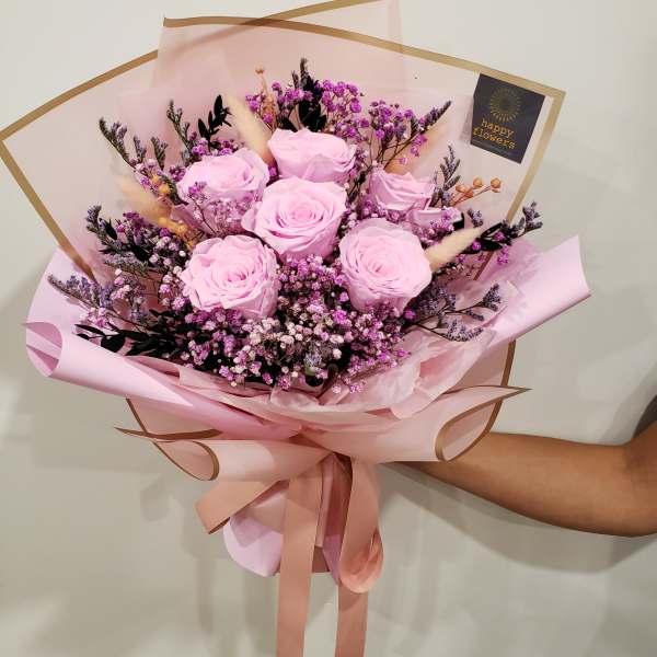 Bouquet of pale pink roses with purple filler flowers wrapped in pink paper