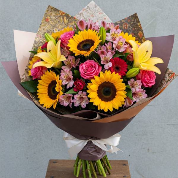 Bouquet of sunflowers, pink roses, lilies, and alstroemeria wrapped in paper