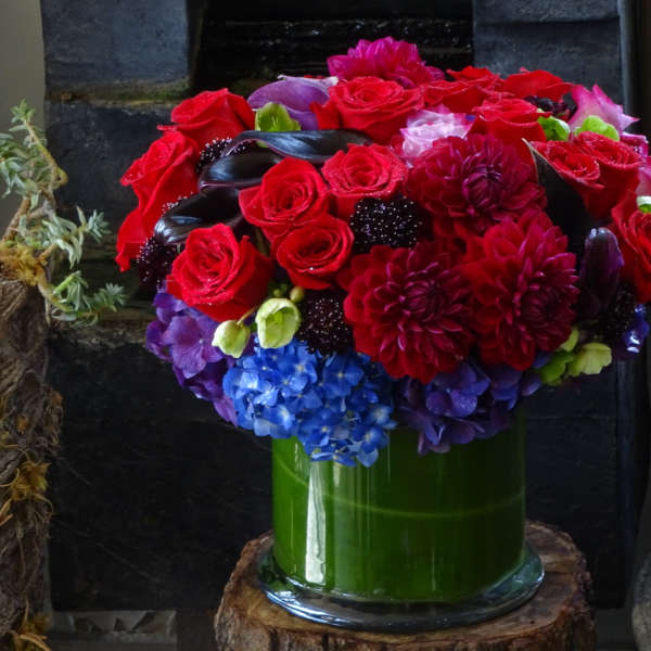 Bouquet of red, purple, and blue flowers in a green glass vase