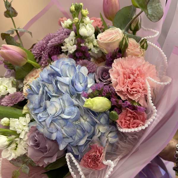 Pastel bouquet with blue hydrangea, pink roses, and purple blooms in pink wrap
