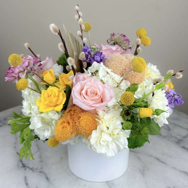 Mixed bouquet of roses, hydrangeas, and yellow pom-pom flowers in a white vase