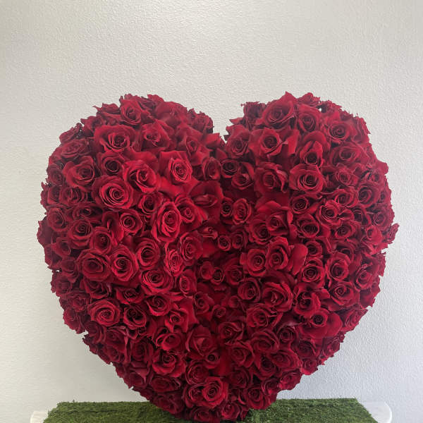 Heart-shaped arrangement of red roses on a moss-covered table