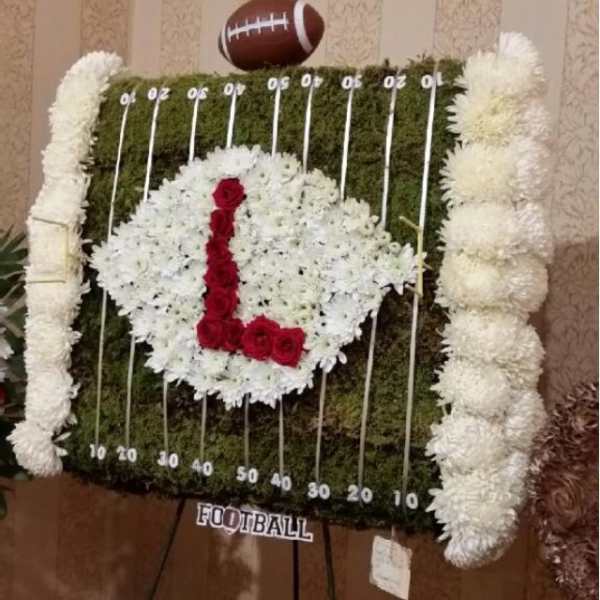 Football-shaped floral display with white flowers and red roses on an easel
