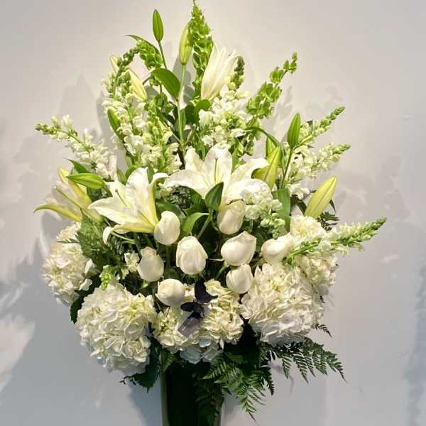 Tall white floral arrangement in a glass vase with lilies and hydrangeas