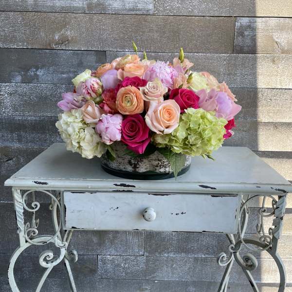 Mixed bouquet of pink, peach, and green flowers in a low container