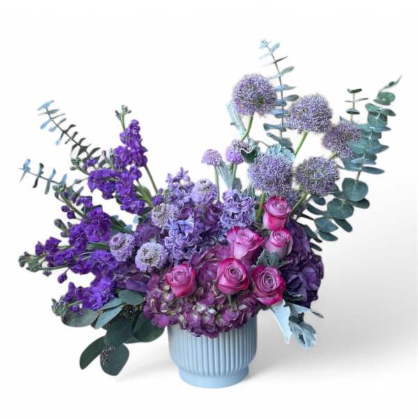Purple and pink floral arrangement in a ribbed blue vase