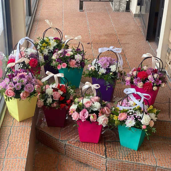 Bright mixed flower arrangements in colorful handled gift boxes with ribbon bows on outdoor steps