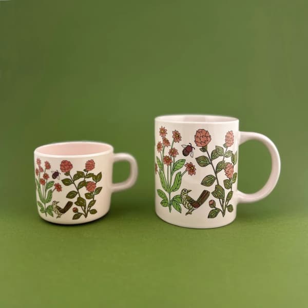 Two floral-print ceramic mugs on a green background