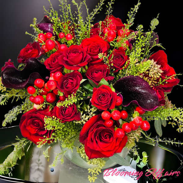 Red roses with dark calla lilies and berry accents in a vase