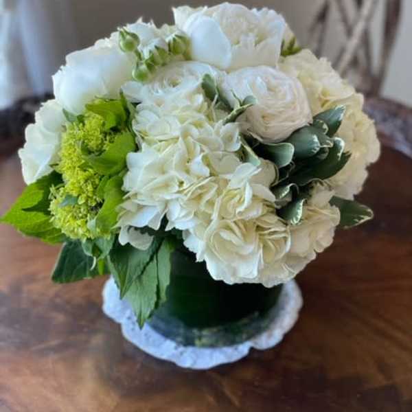 White floral arrangement in a dark vase with green accents