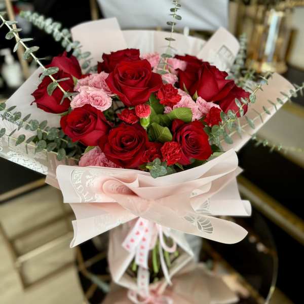 Bouquet of red roses and pink carnations wrapped in pale pink paper