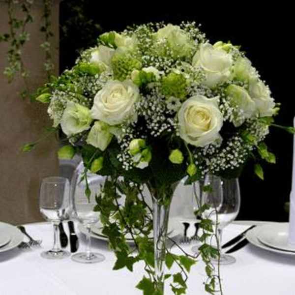 White rose centerpiece in a tall glass vase on a table