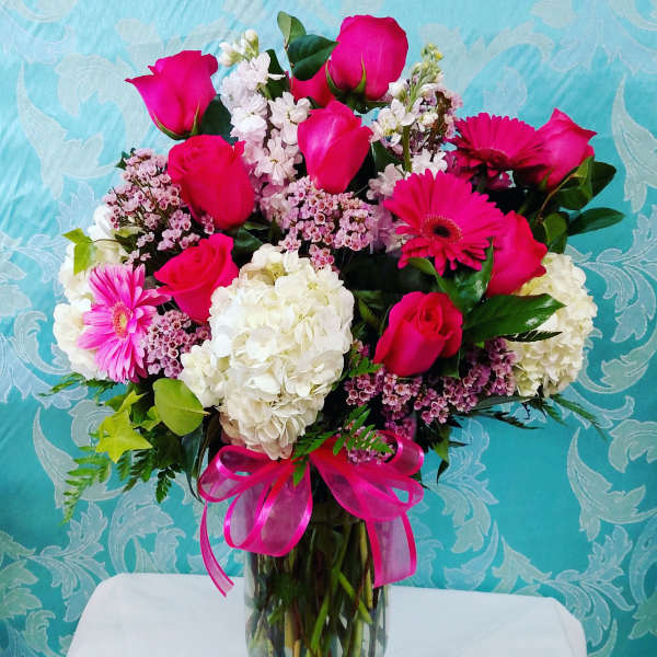 Bouquet of pink roses, gerbera daisies, and white hydrangeas in a glass vase