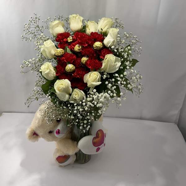 Red and white rose bouquet with baby’s breath in a glass vase and teddy bear