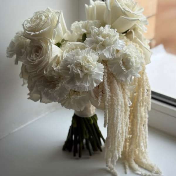 White bridal bouquet with roses and ruffled blooms, finished with trailing strands