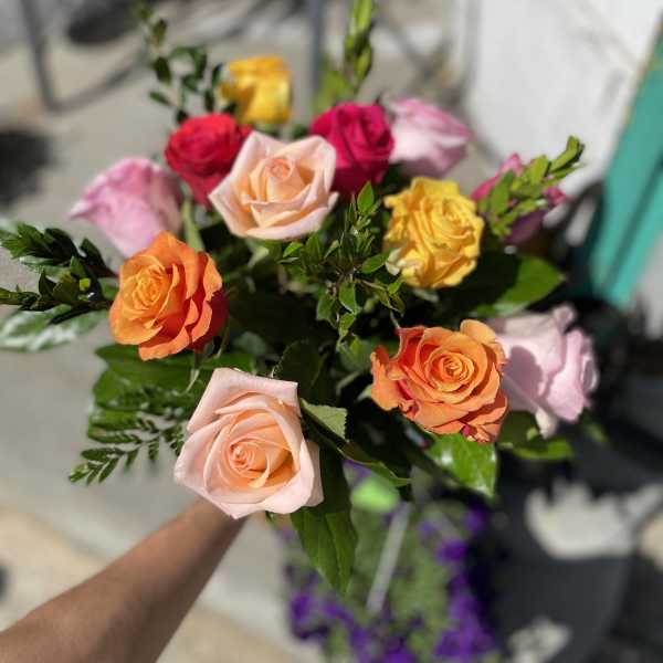 Handheld bouquet of multicolored roses with greenery