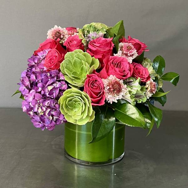 Pink roses and purple hydrangea in a green glass vase