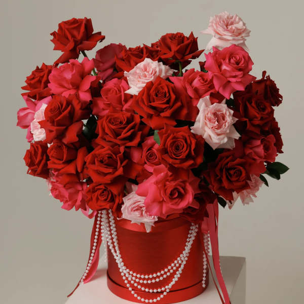 Large bouquet of red and pink roses in a red hatbox with pearl strands