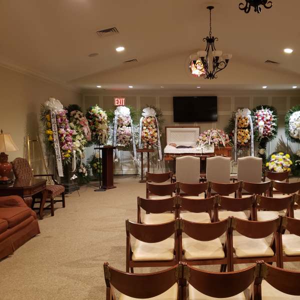 Funeral chapel with floral sprays around an open casket and rows of chairs