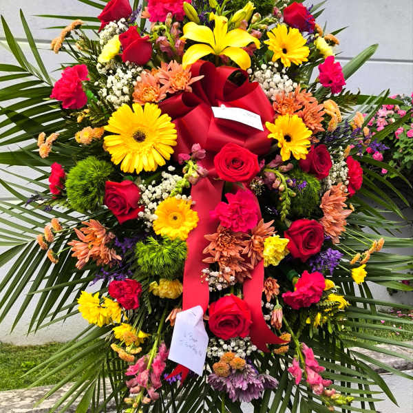 Large standing floral spray with red roses and yellow lilies on a red ribboned easel