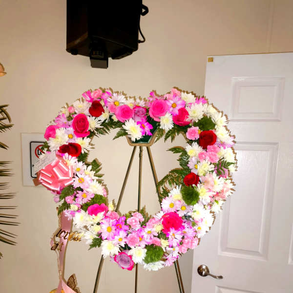 Heart-shaped floral wreath on a stand with pink, white, and red flowers