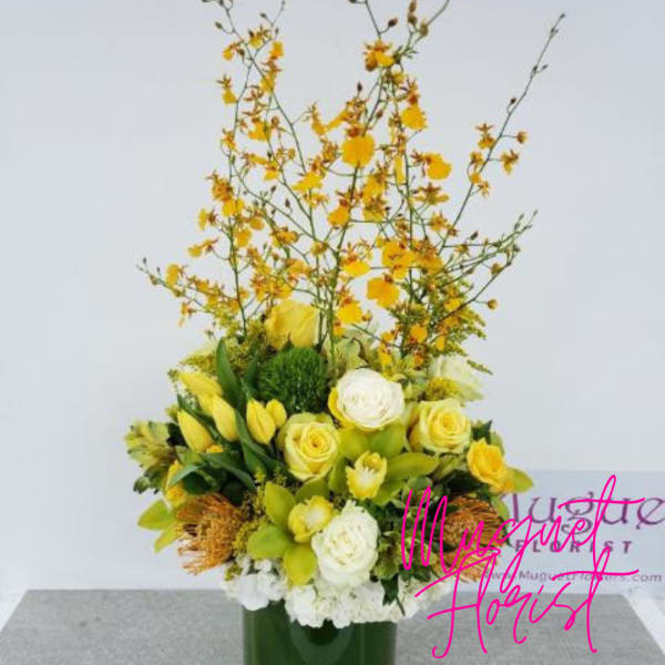 Yellow and white floral arrangement in a green vase with tall branching stems