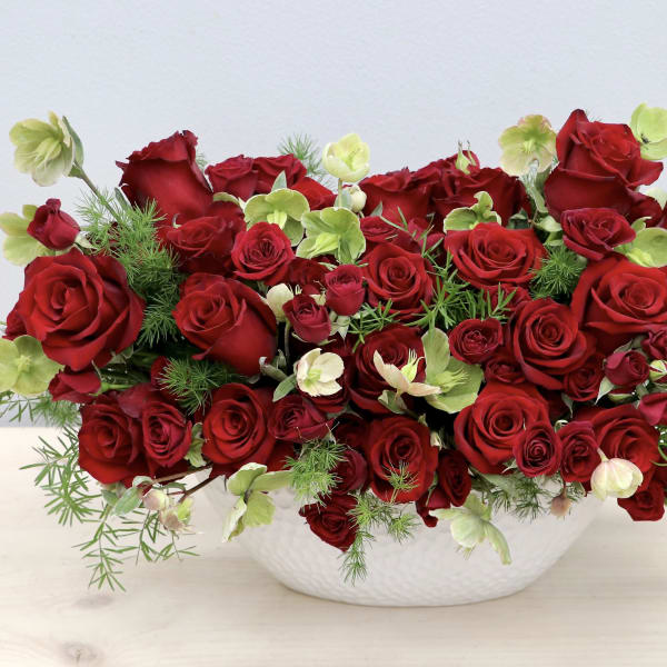 Red roses arranged in a white bowl with pale green accents