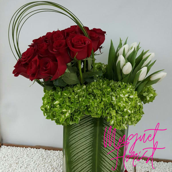 Red roses and white tulips in a tall green vase with green hydrangeas