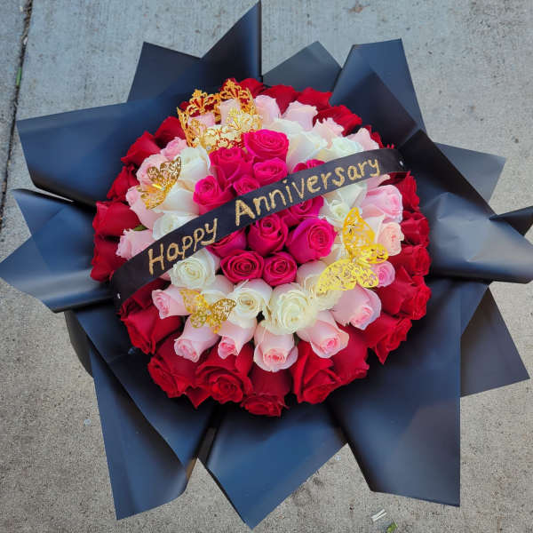 Round bouquet of red, pink, and white roses with a Happy Anniversary ribbon