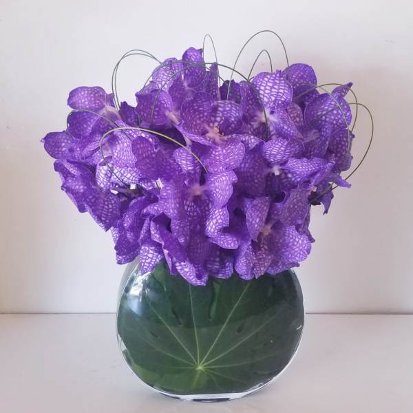 Purple orchid arrangement in a round glass vase