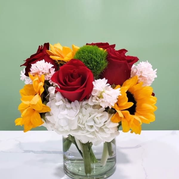 Bouquet of red roses, yellow sunflowers, and white hydrangeas in a glass vase