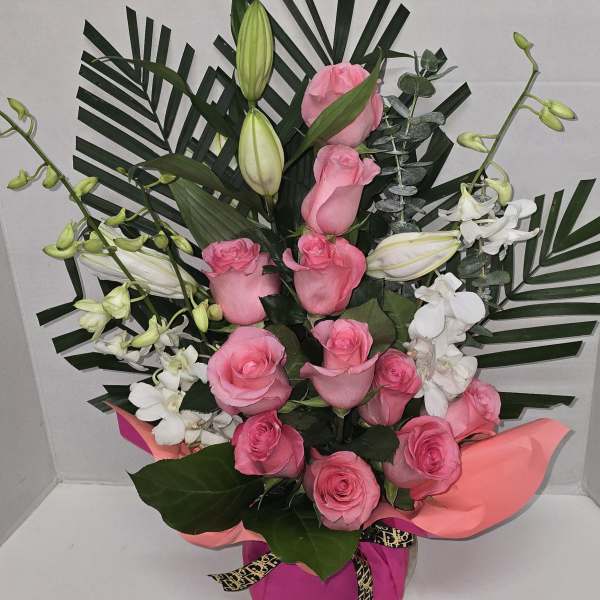 Pink roses and white lilies arranged with palm leaves in a gift box