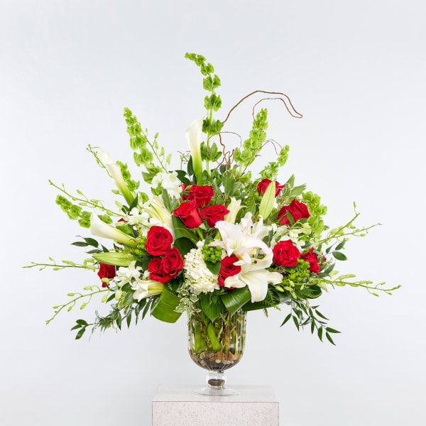 Red roses and white lilies in a glass vase with tall green accents