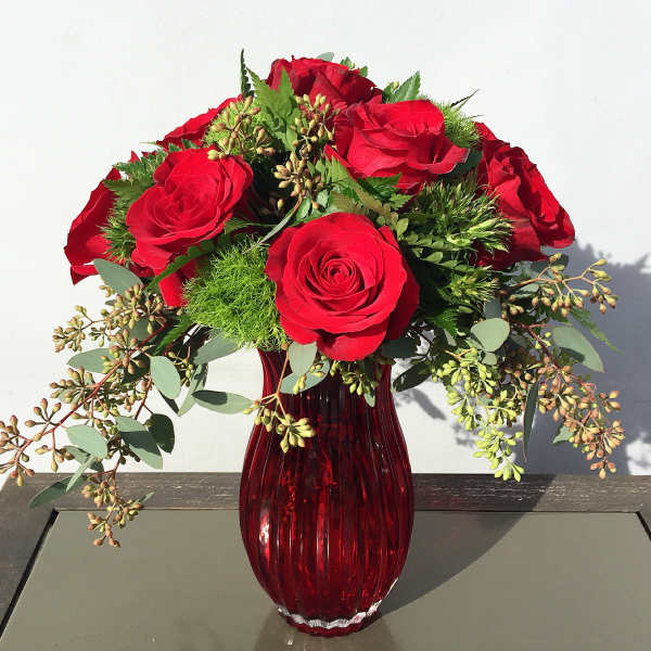 Red roses arranged in a red glass vase with greenery