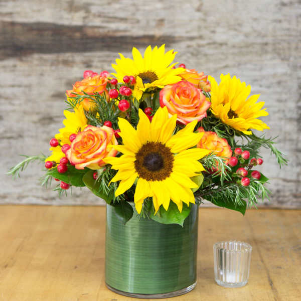 Sunflowers and orange roses in a green glass vase
