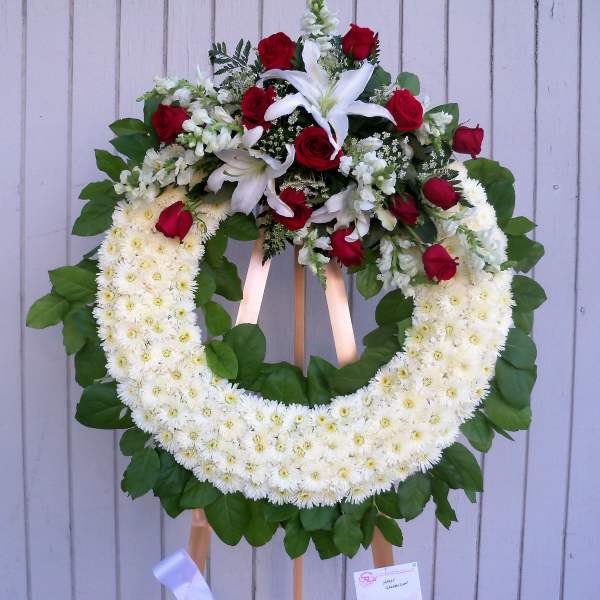 Large floral wreath with white daisies, red roses, and white lilies on an easel